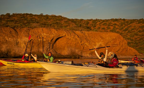 A group of female students out sea kayaking by rock bluffs at sunset on the Sea of Cortez in Baja California, Mexico.   