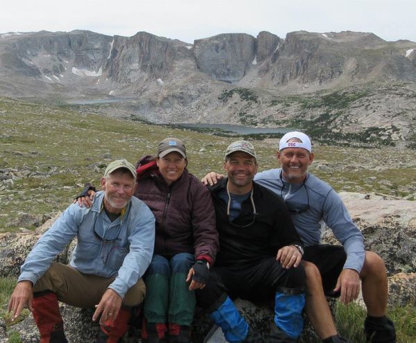 Four students on a NOLS Custom Education course smile together for a picture with mountains in the background.