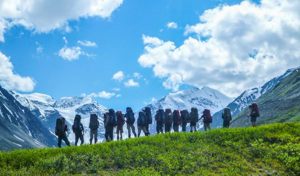 Students standing on a green grassy hill in Alaska - while out backpacking - and looking off to snow capped mountains in the distance.